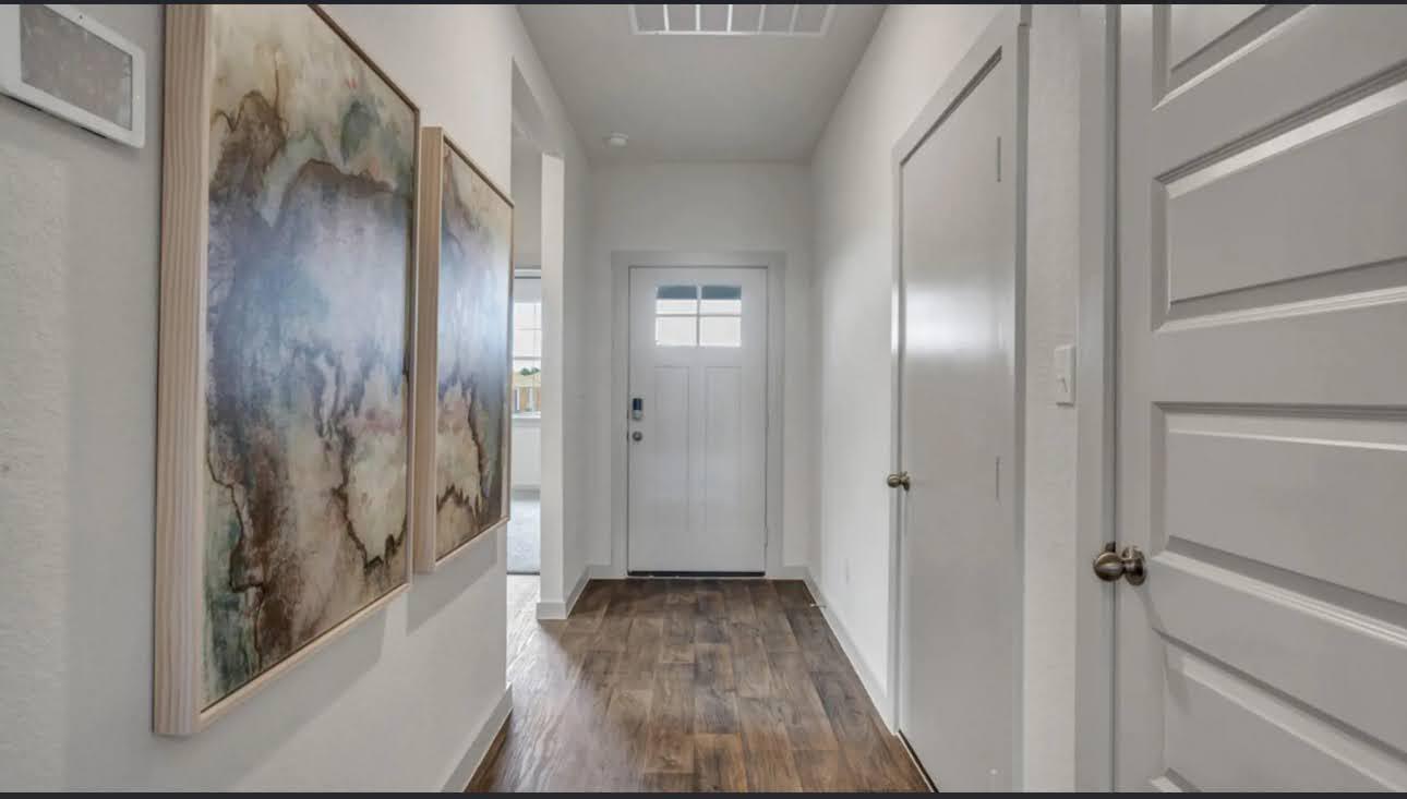 Entry hallway with wood-look flooring, framed abstract art, and a white front door.