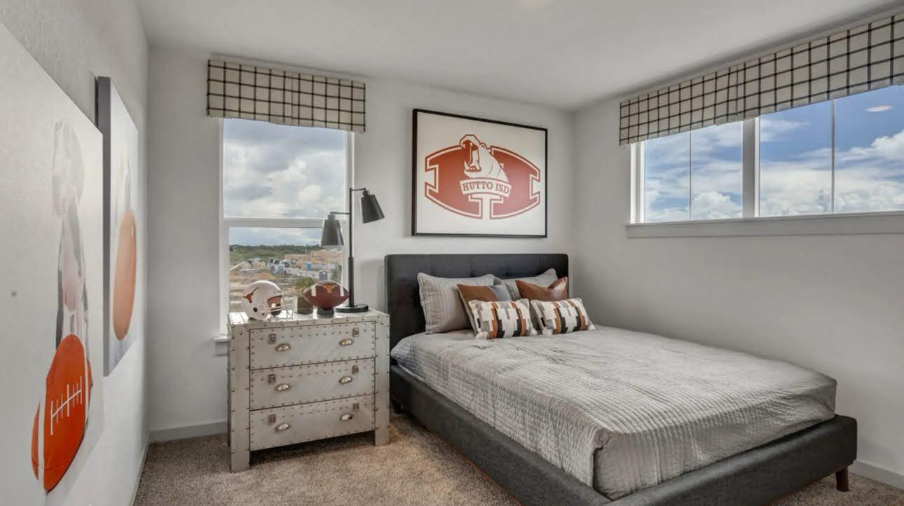 Bedroom with a gray bed, football-themed decor, and windows overlooking a neighborhood.