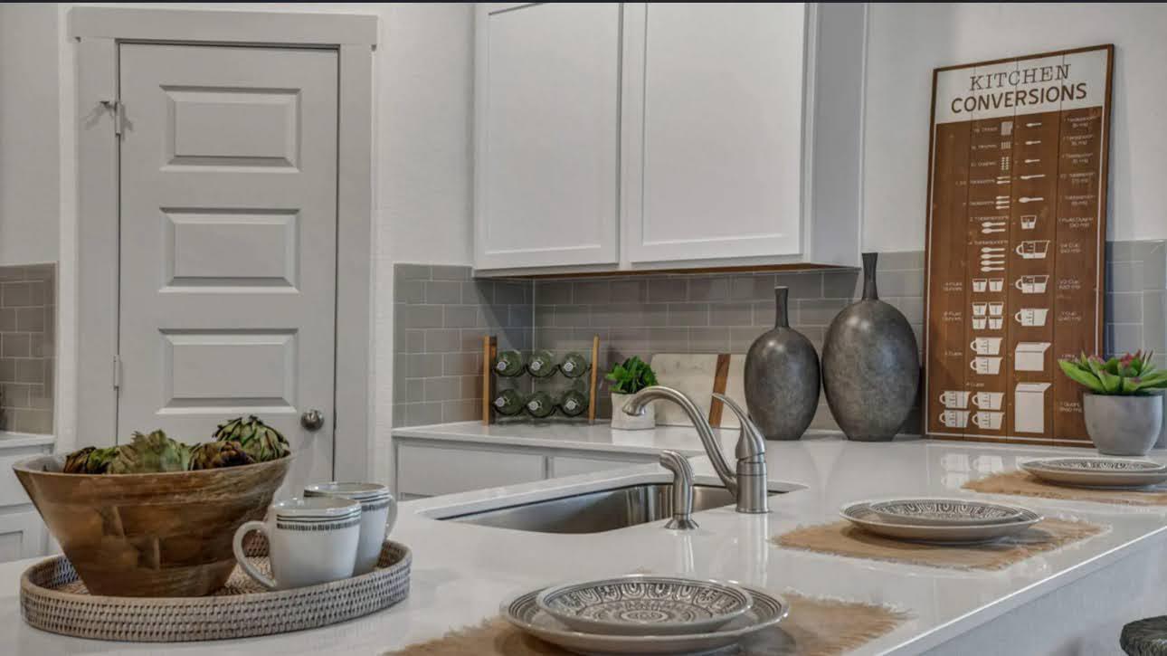 Staged kitchen with white cabinets, gray tile backsplash, and a countertop sink.