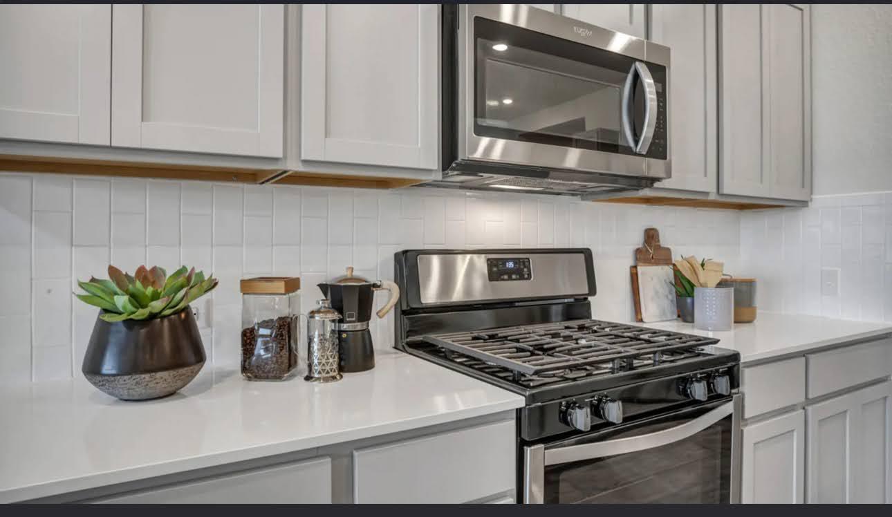 Kitchen with white shaker cabinets, light counters, and a stainless steel gas range and microwave.