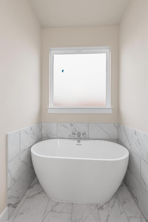 Bathroom with a freestanding white soaking tub, marble-look tile, and a window.