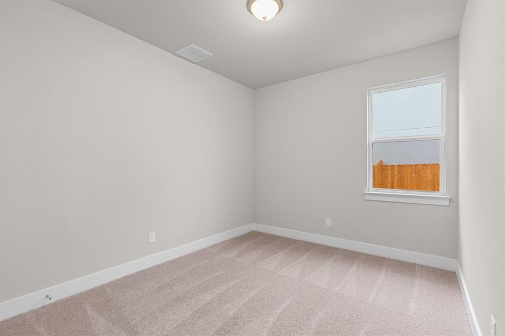 Empty carpeted bedroom with neutral walls and a window overlooking a wooden fence.