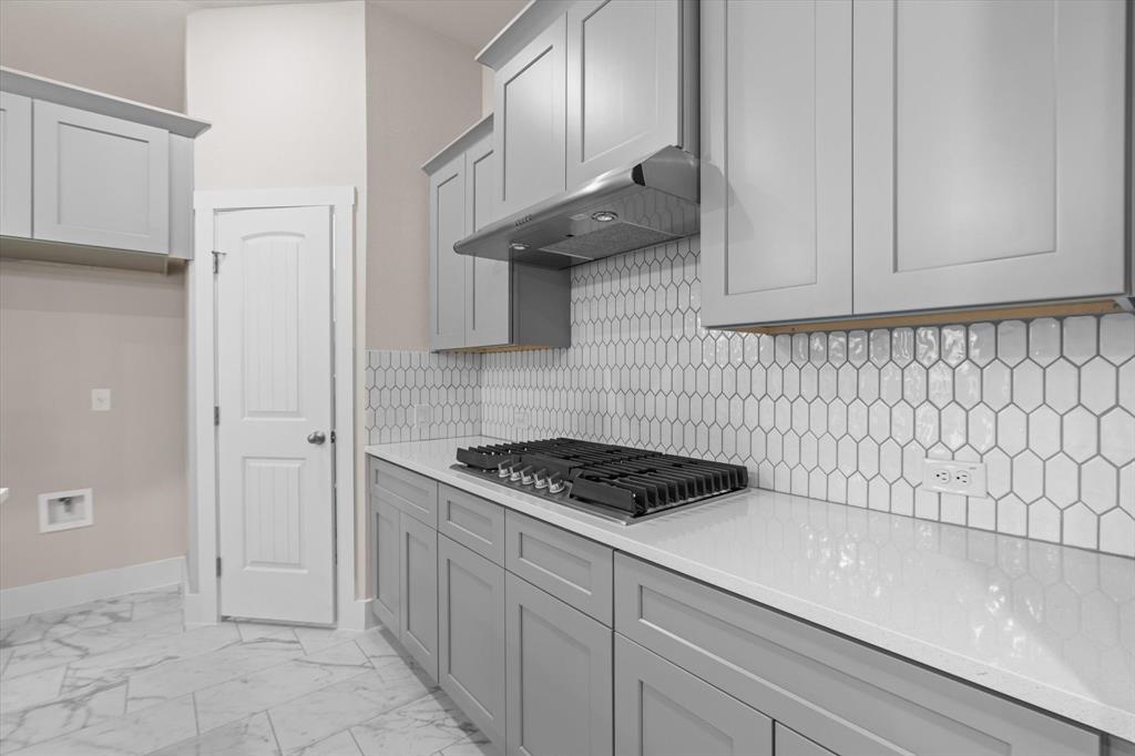 Kitchen with a gas cooktop, white hexagonal backsplash, and marble-look tile flooring.