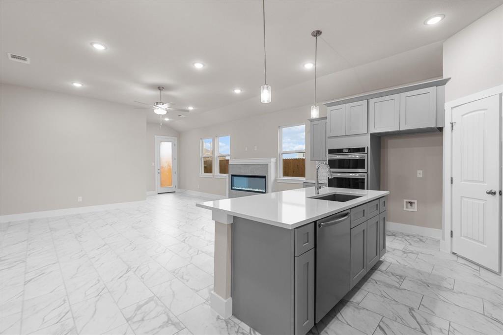 Open kitchen with a large white island, gray cabinets, marble-look tile, and a fireplace.