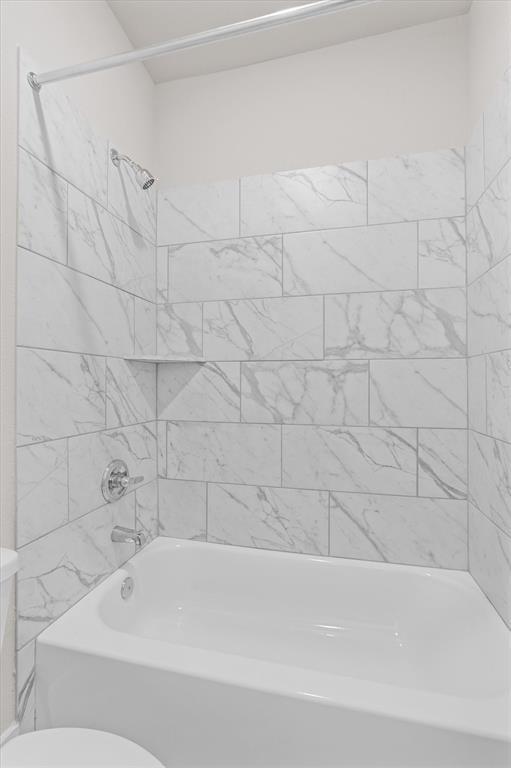 Bathroom tub and shower with marble-look tile walls and chrome fixtures.
