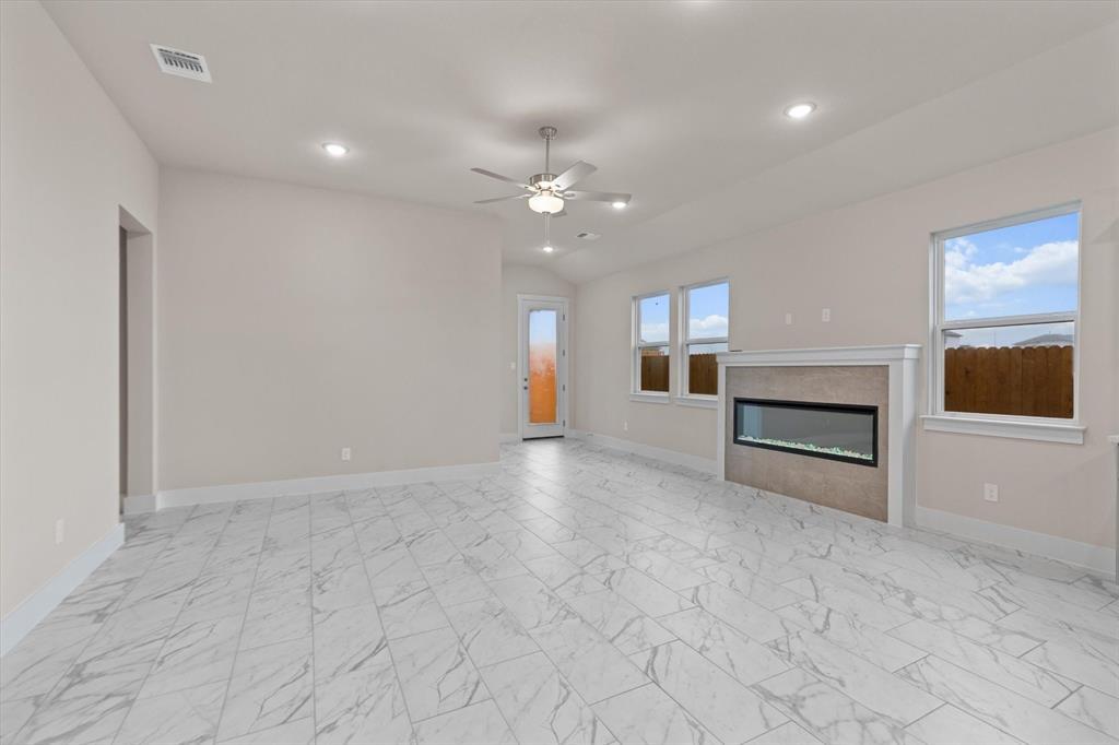 Empty living room with marble-look tile floors, a modern fireplace, and windows facing a fenced yard.