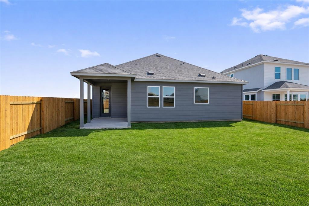 Gray home with a covered rear patio, fenced yard, and broad green lawn.