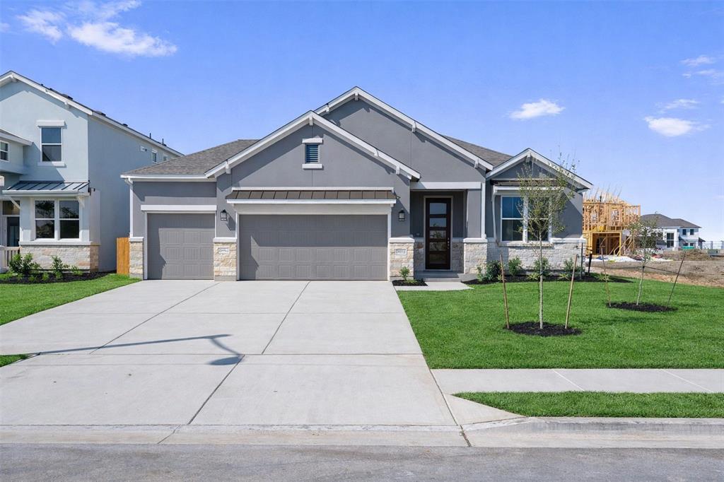 Gray single-story home with stone accents, a three-car garage, and a wide concrete driveway.