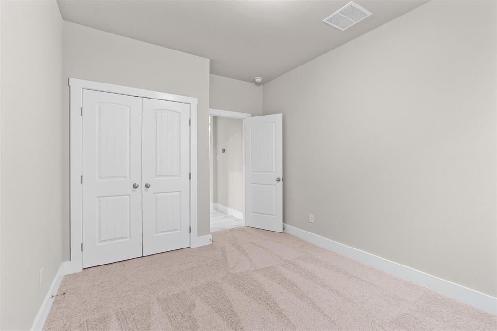 Empty bedroom with beige carpet, double white closet doors, and an open doorway to a tiled hall.