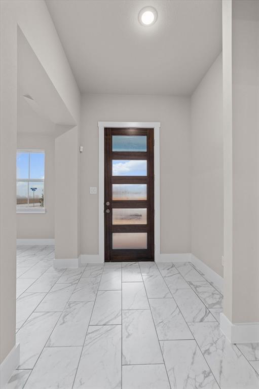 Empty entry foyer with marble-look tile flooring and a dark wood door with glass panels.