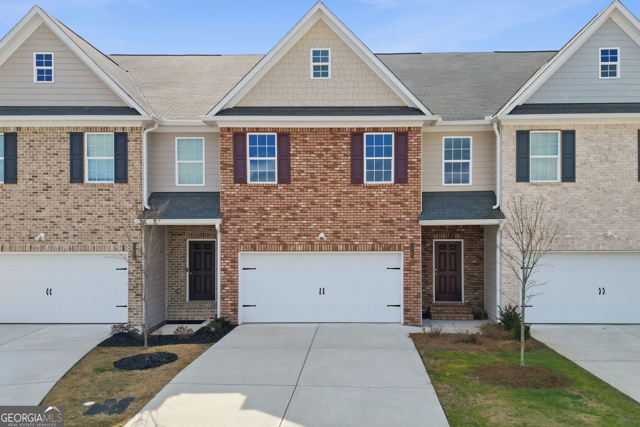 Two-story brick townhome with a white double garage door and a concrete driveway.