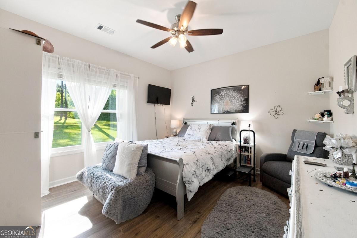 Furnished bedroom with a gray bench, recliner, and sunlit window with sheer curtains.