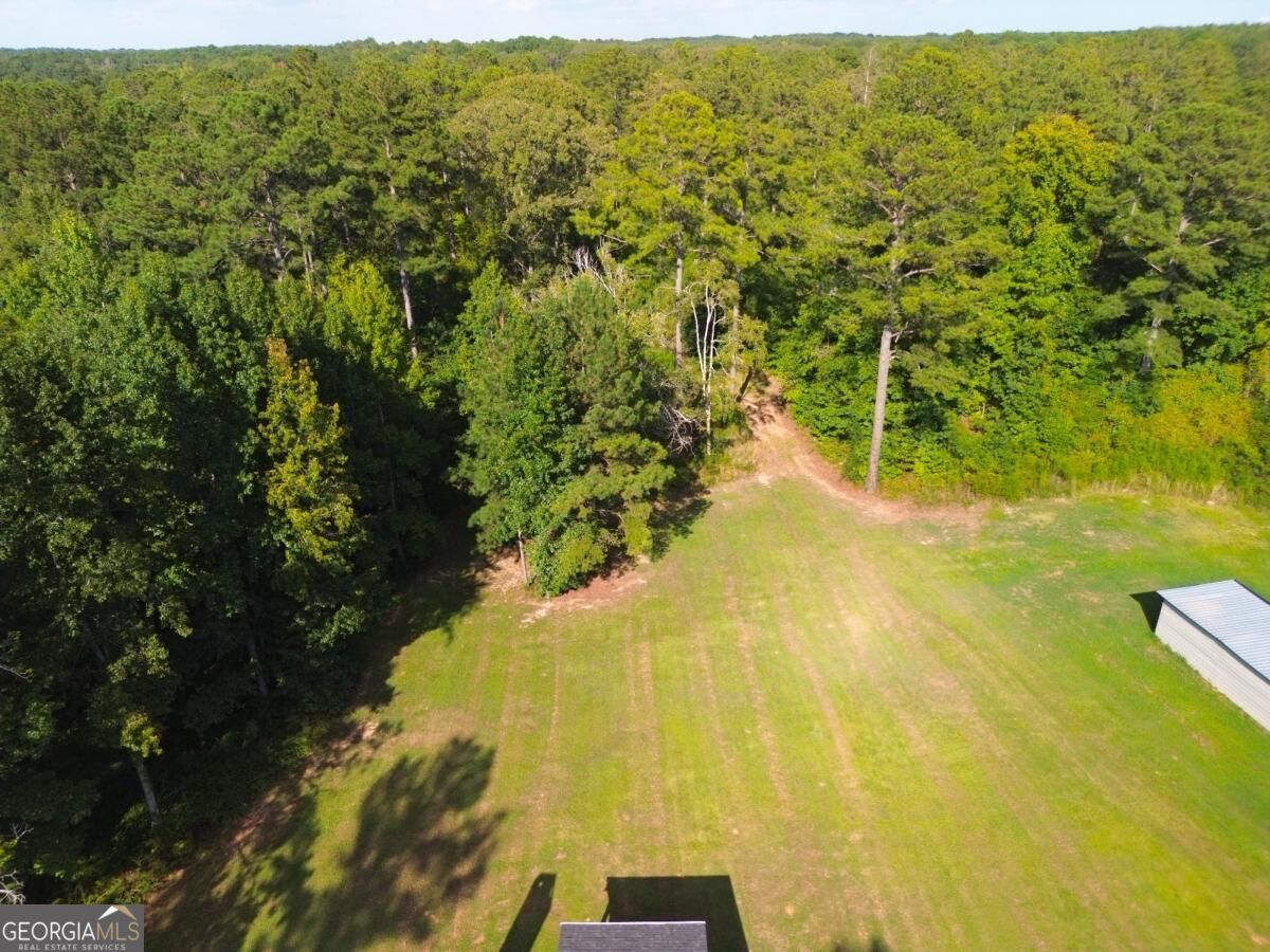 Aerial view of a grassy clearing bordered by dense woods, with a metal-roofed outbuilding at the edge.