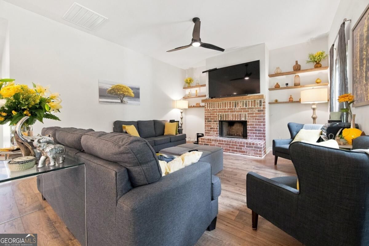 Living room with gray seating, a brick fireplace, and a large TV above the mantel.