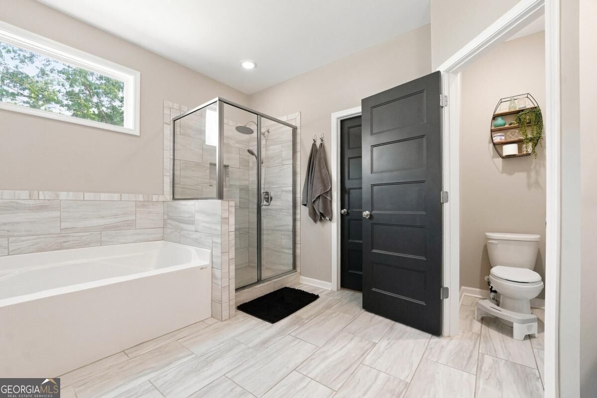 Bathroom with a tiled bathtub, glass-enclosed shower, and separate toilet alcove.