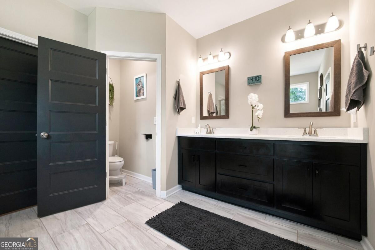 Bathroom with a long dark double vanity, two mirrors, and pale tile flooring.