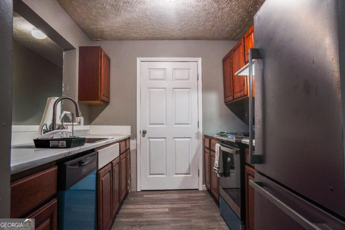 Galley kitchen with reddish-brown cabinets, white counters, and stainless-steel appliances.