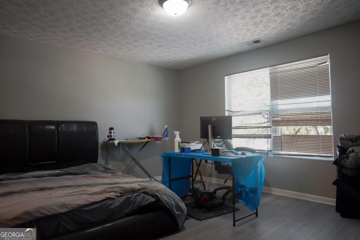 Bedroom with a dark upholstered bed, rumpled bedding, and a desk beside a large window.