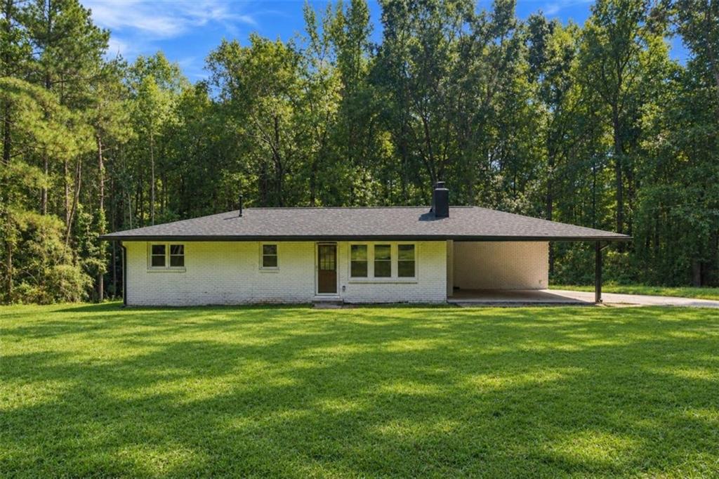 White brick ranch house with an attached carport, broad lawn, and mature trees.