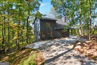 Dark gray two-story house among trees, viewed from its broad paved driveway.