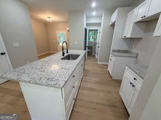 Kitchen with a large granite island, white cabinetry, and light wood flooring.