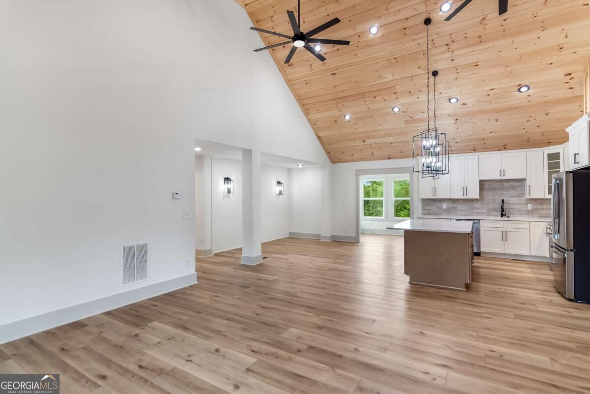 Open-plan kitchen and living area beneath a vaulted wood ceiling, with white cabinets and a central island.