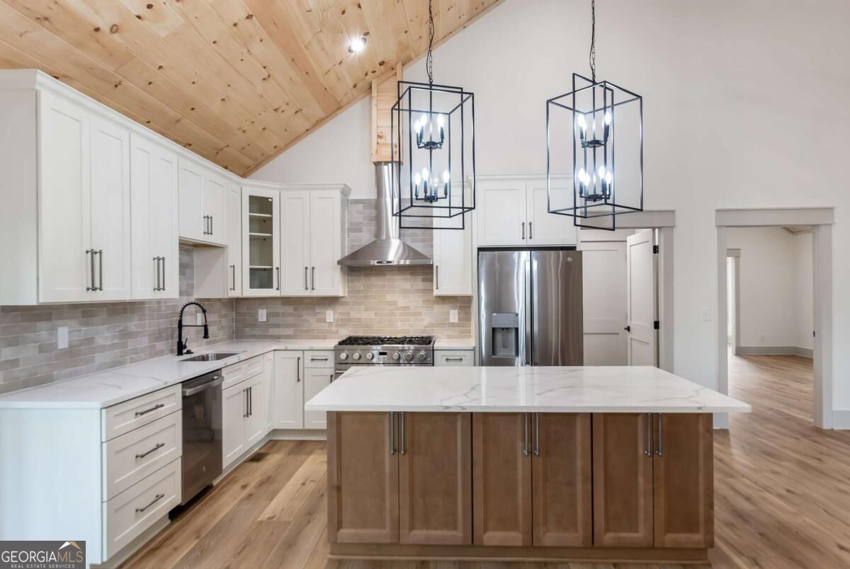 Kitchen with a large wood-paneled island, white cabinets, stainless steel appliances, and a vaulted wood ceiling.