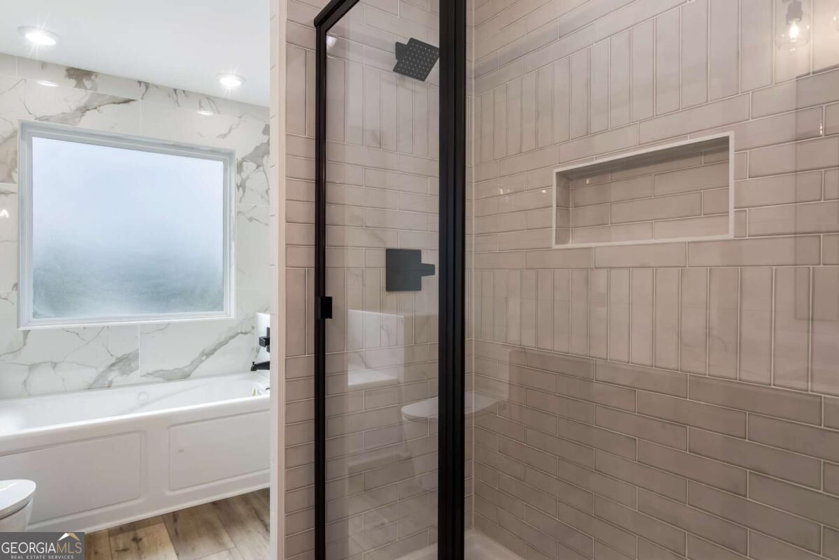 Bathroom with a tiled glass shower and recessed niche beside a bathtub and frosted window.