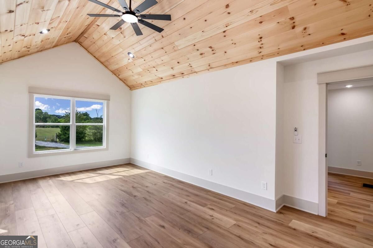 Empty room with a vaulted wood ceiling, ceiling fan, and wide window overlooking greenery.