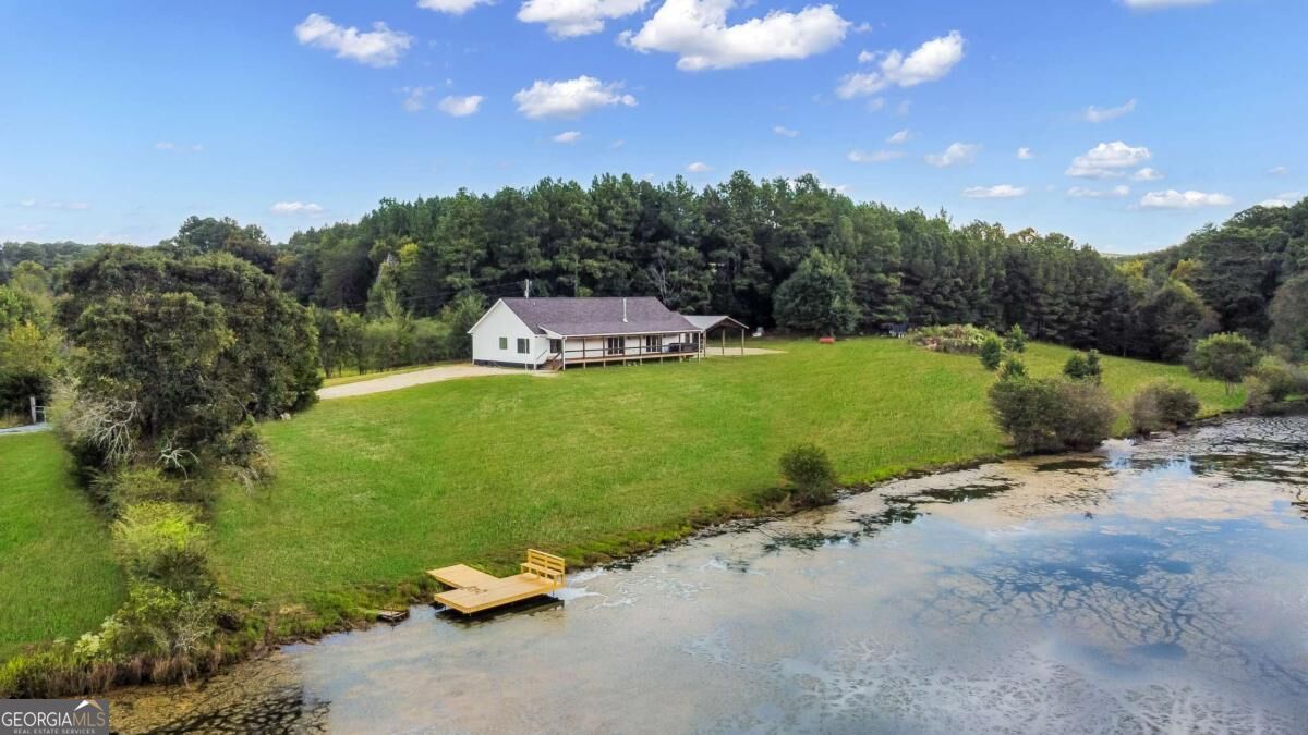 Aerial view of a home beside a lake, with a broad lawn and small dock.