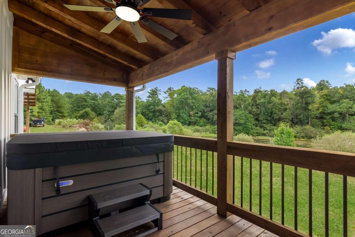 Covered wooden deck with a hot tub overlooking a grassy yard and wooded landscape.