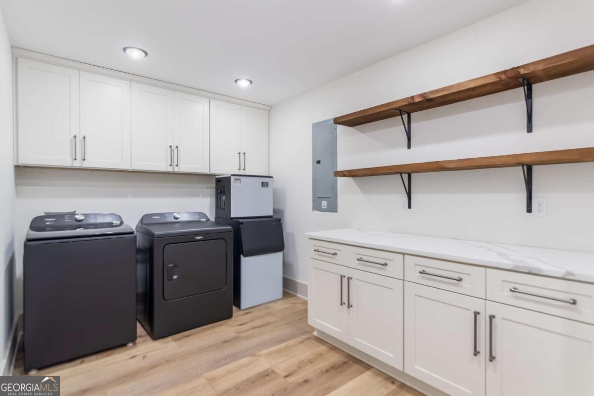 Laundry room with dark washer and dryer, white cabinetry, and long wooden shelves.