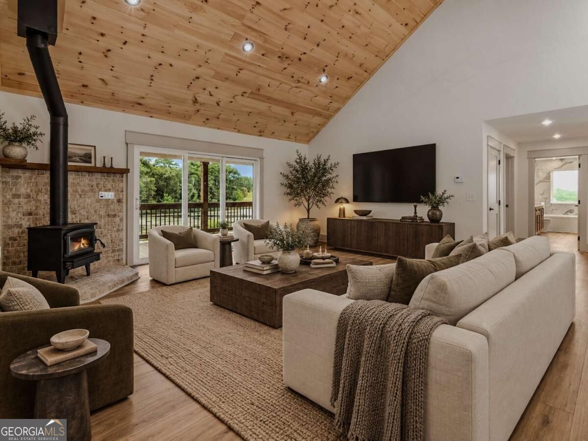 Living room with a vaulted pine ceiling, wood stove, and sliding doors opening to a deck.
