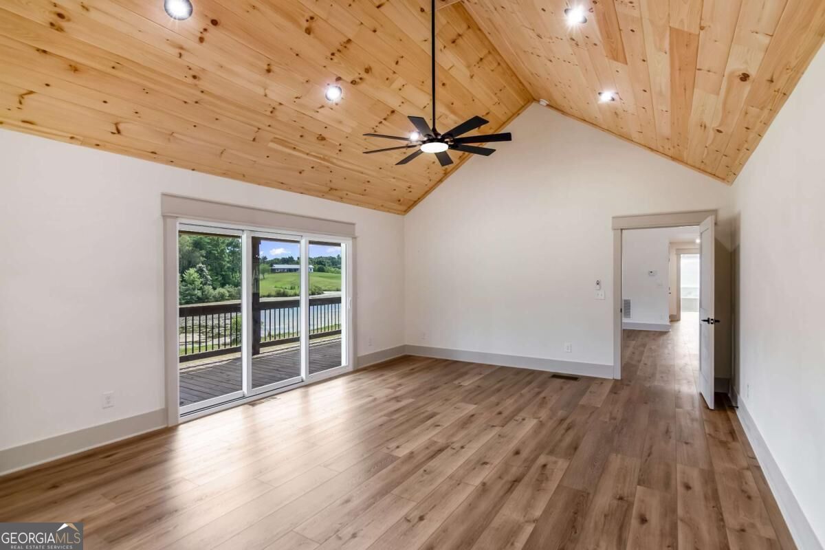 Vacant room with a vaulted wood ceiling, wood-look floors, and sliding doors to a deck.