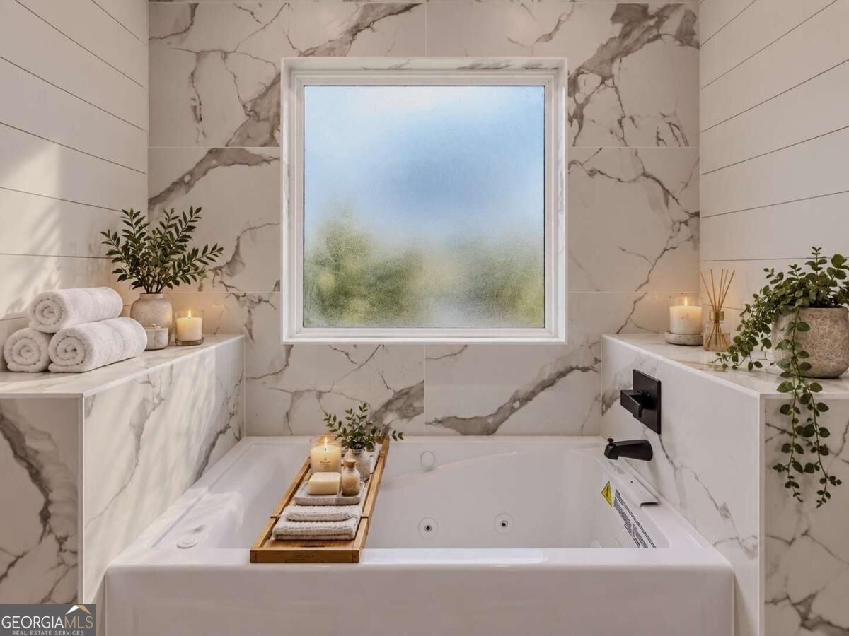 Jetted bathtub beneath a frosted window, framed by marble-look tile and decorated with towels and candles.