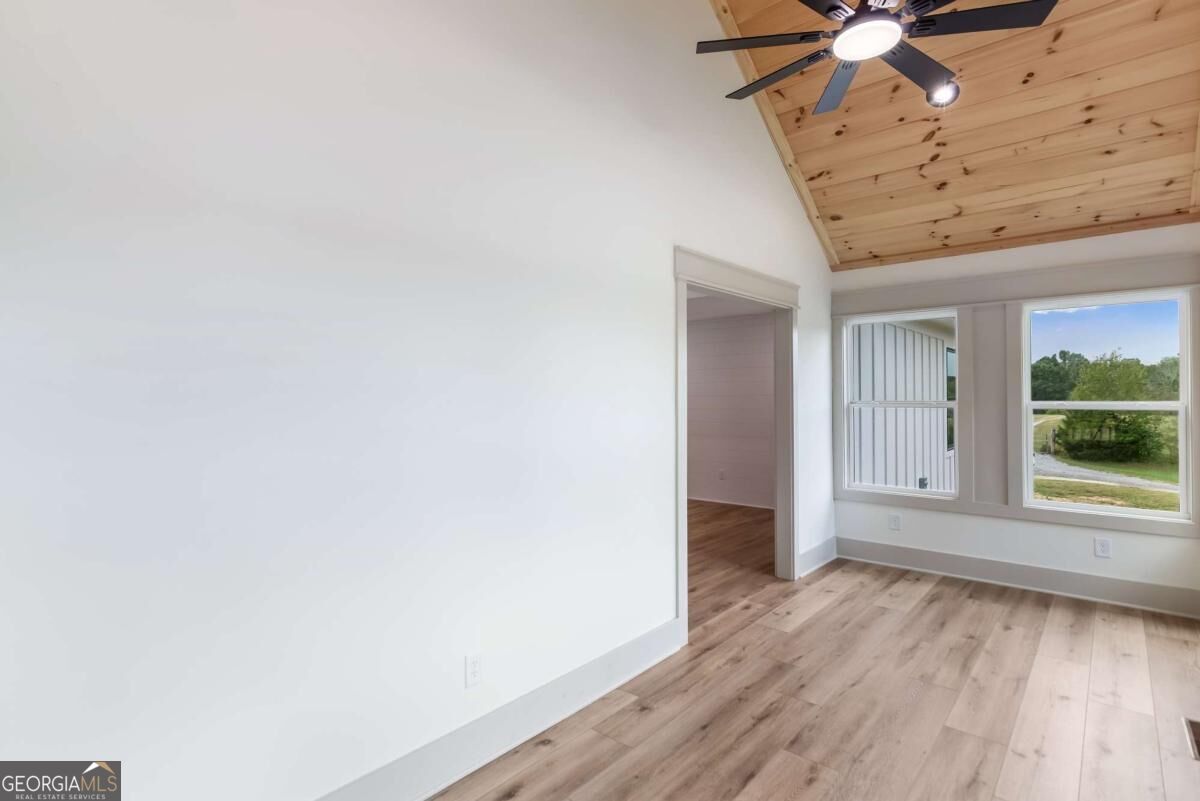 Vacant room with a vaulted wood-plank ceiling, ceiling fan, and windows overlooking a green landscape.