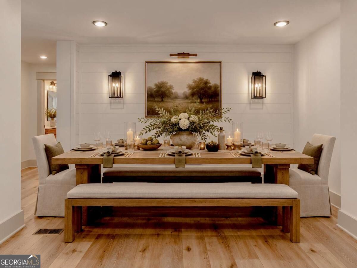 Staged dining room with a candlelit wooden table, upholstered seating, and framed landscape art.