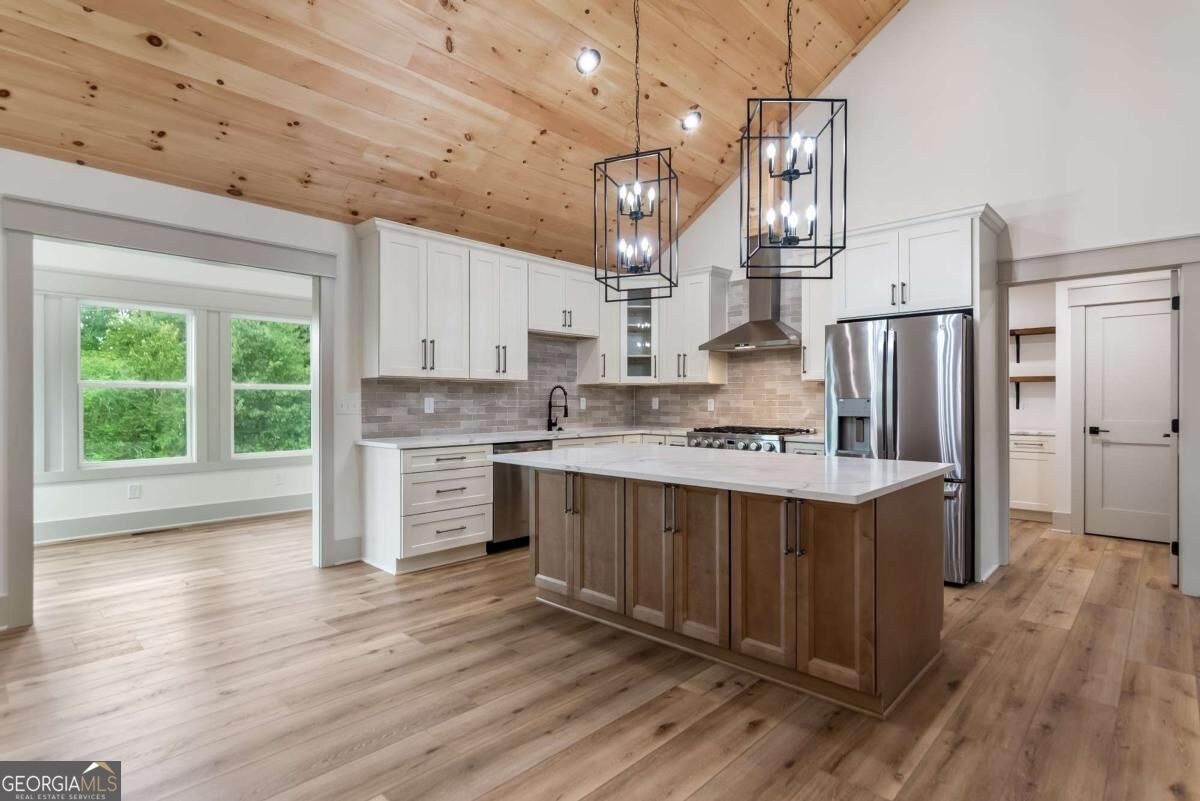 Kitchen with a large wood-paneled island, white cabinets, stainless appliances, and a vaulted wood ceiling.