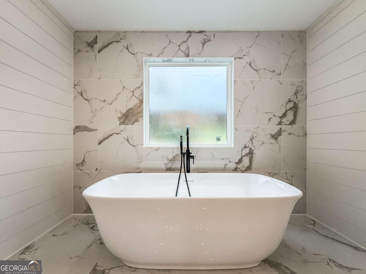 Bathroom with a freestanding tub, black floor-mounted faucet, marble-look tile, and frosted window.