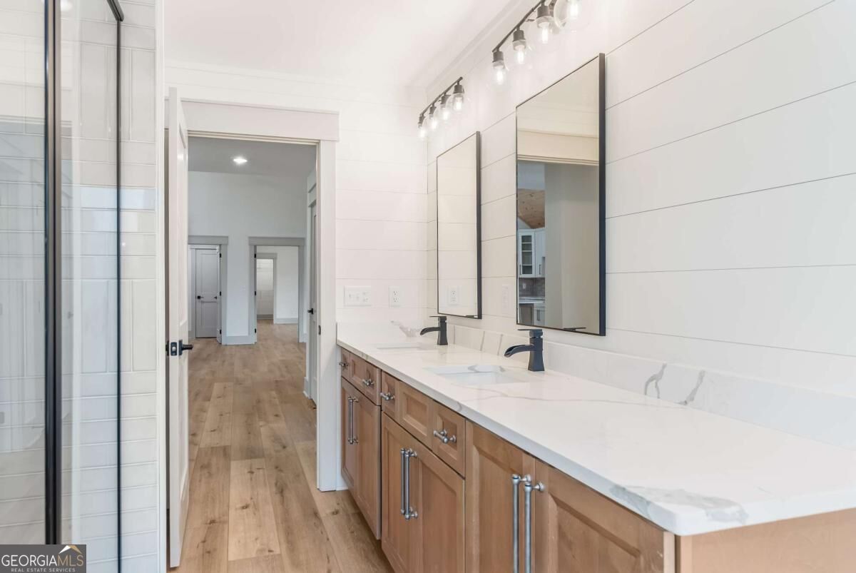 Bathroom with a long double vanity, wood cabinets, two mirrors, and a glass-enclosed shower.
