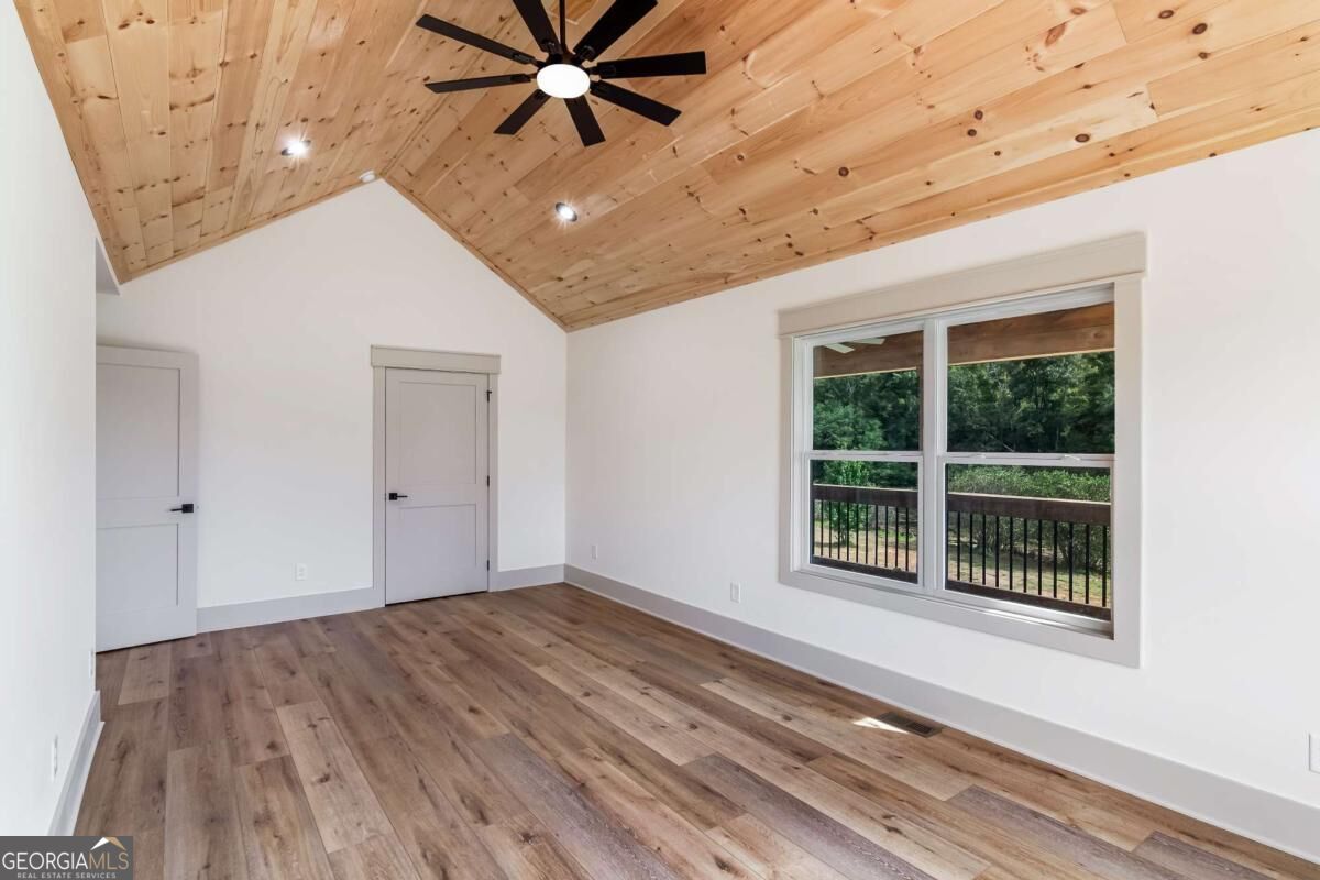 Vacant room with a vaulted pine ceiling, ceiling fan, and window overlooking a wooded deck.