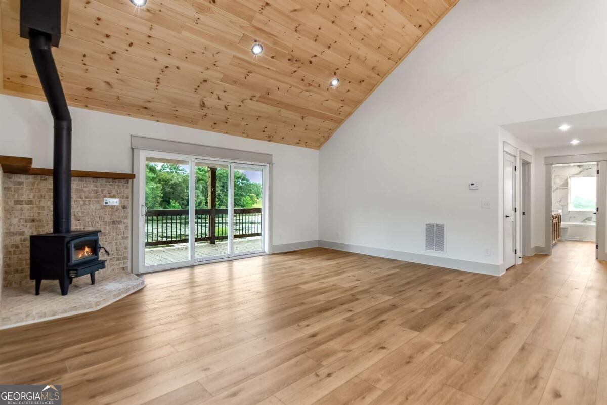 Empty living room with a vaulted wood ceiling, black wood stove, and sliding doors to a deck.