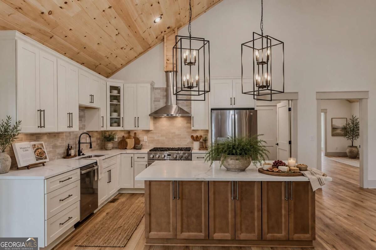 Staged kitchen with a large wood-paneled island, white cabinets, and a vaulted natural-wood ceiling.