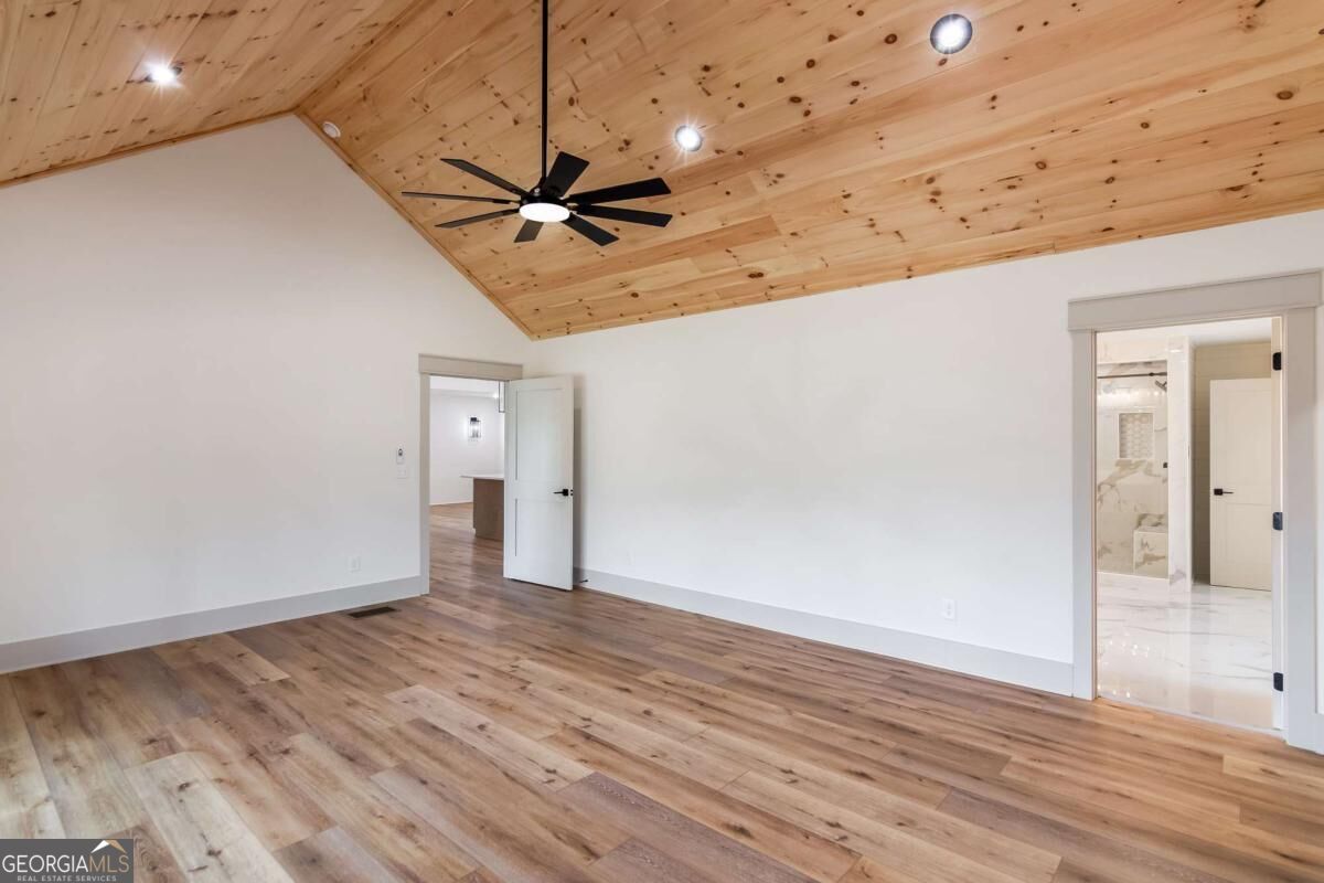 Vacant room with a vaulted wood ceiling, black ceiling fan, and wood plank flooring.