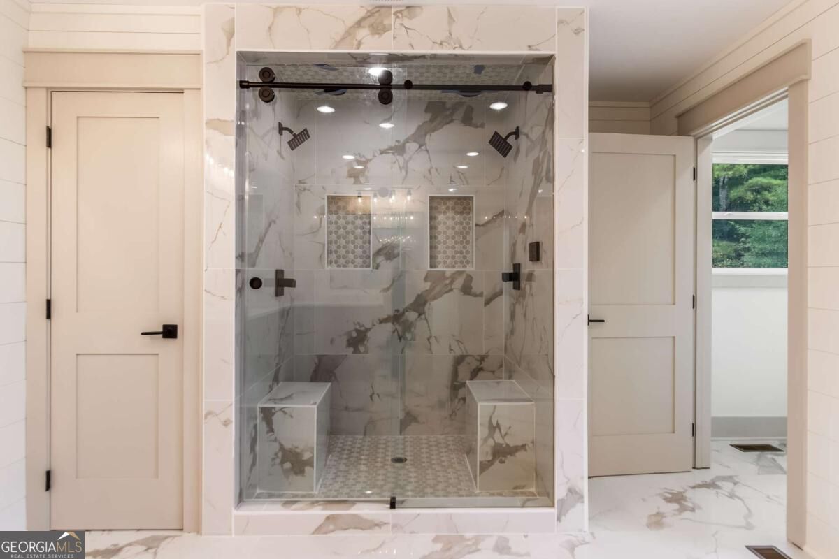 Walk-in shower with marble-look tile, dual showerheads, built-in benches, and a mosaic floor.