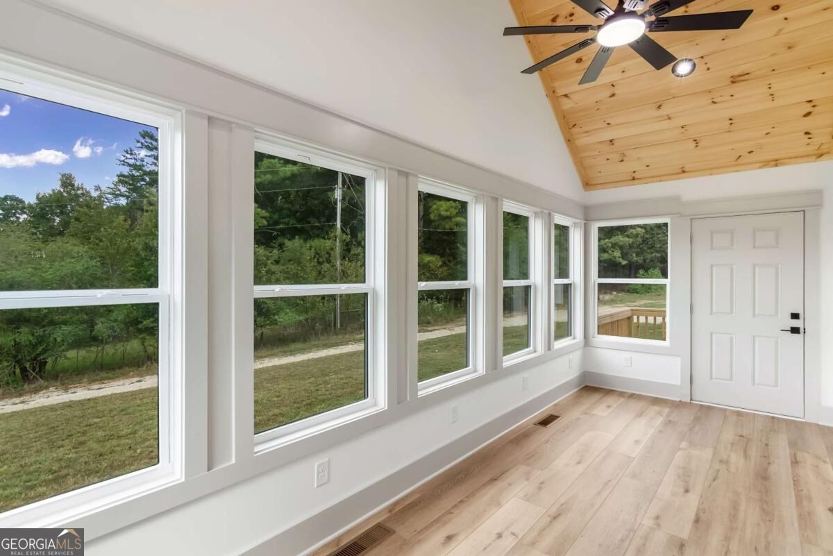 Empty sunroom with large windows, light wood flooring, and a vaulted wood-plank ceiling.