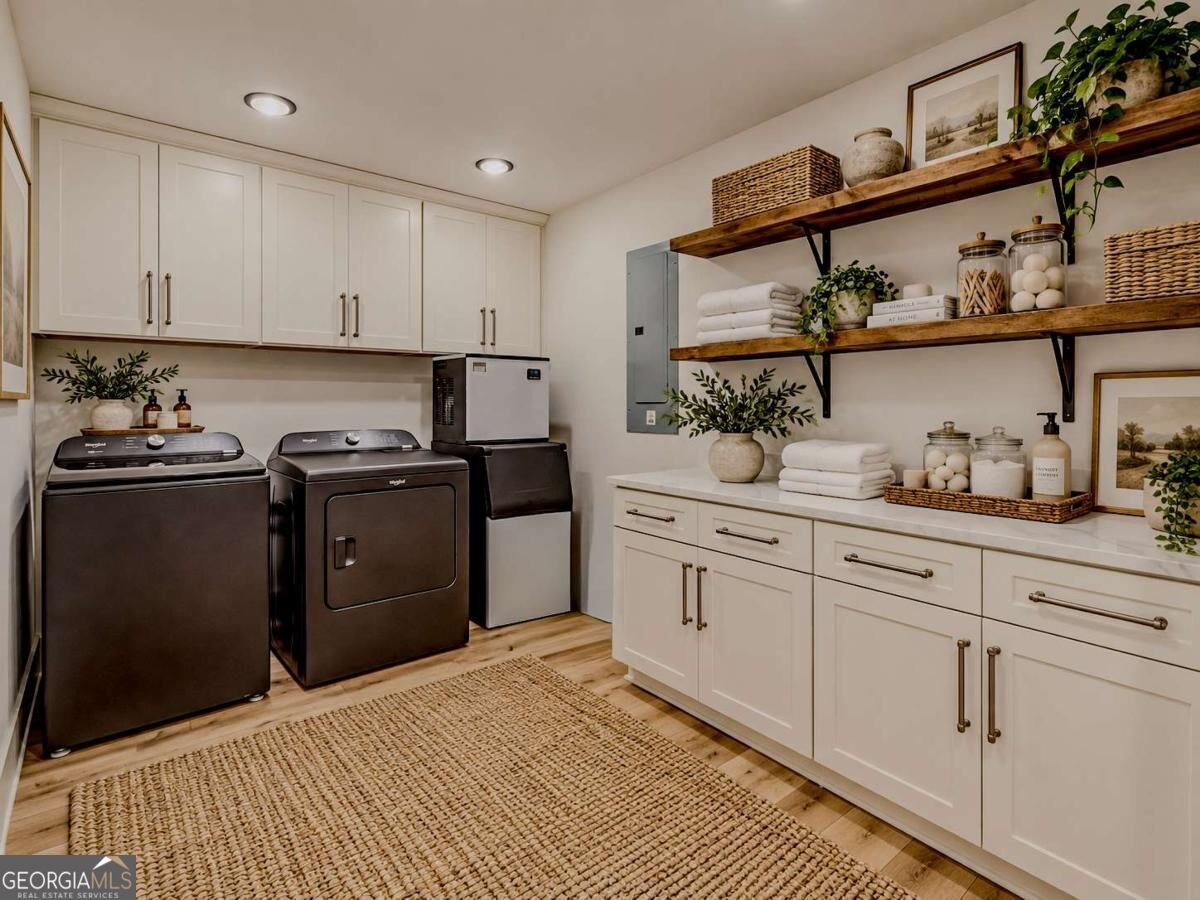 Laundry room with dark washer and dryer, white cabinetry, and open wooden shelves.