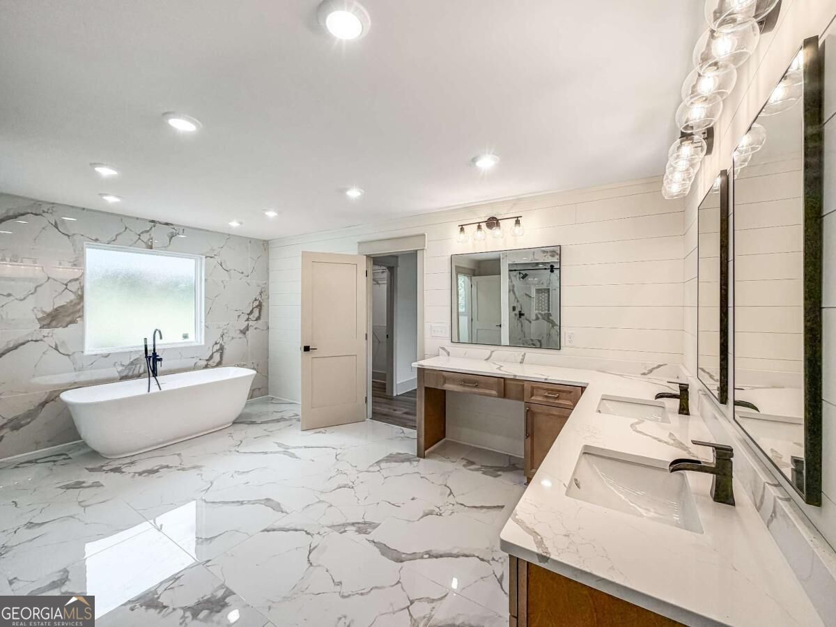 Bathroom with a freestanding tub, marble-patterned surfaces, and a long double-sink vanity.