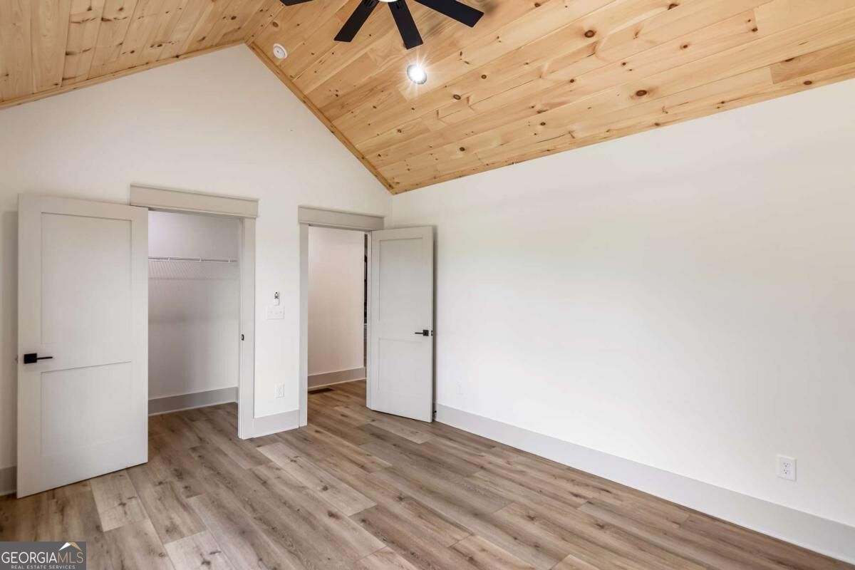 Vacant room with a vaulted wood ceiling, plank flooring, and an open closet.