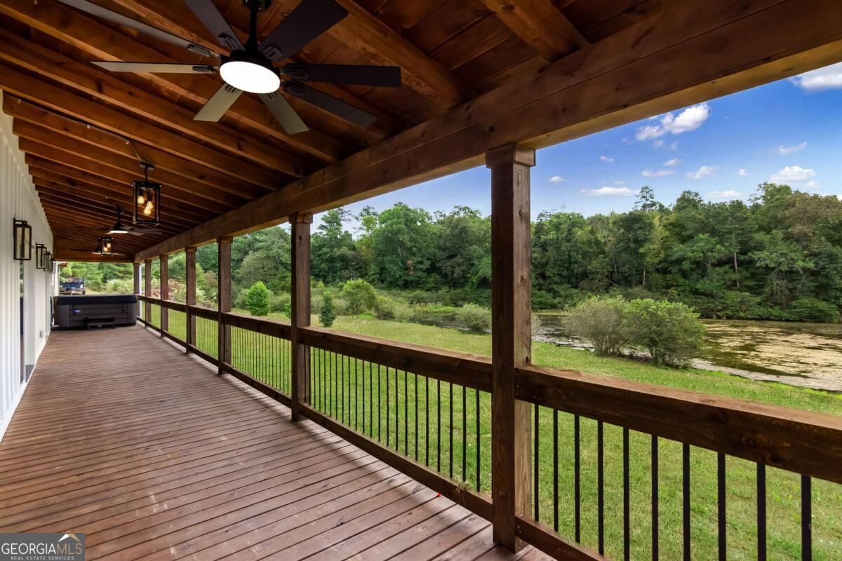 Covered wooden deck overlooks a pond, with a hot tub at the far end.